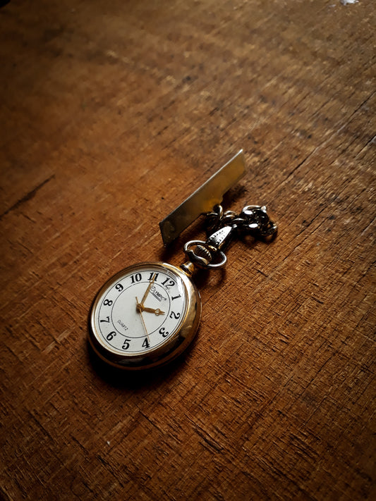 Black Chitsulo gold pocket watch made by Olympic. Black and gold variant on wooden table.